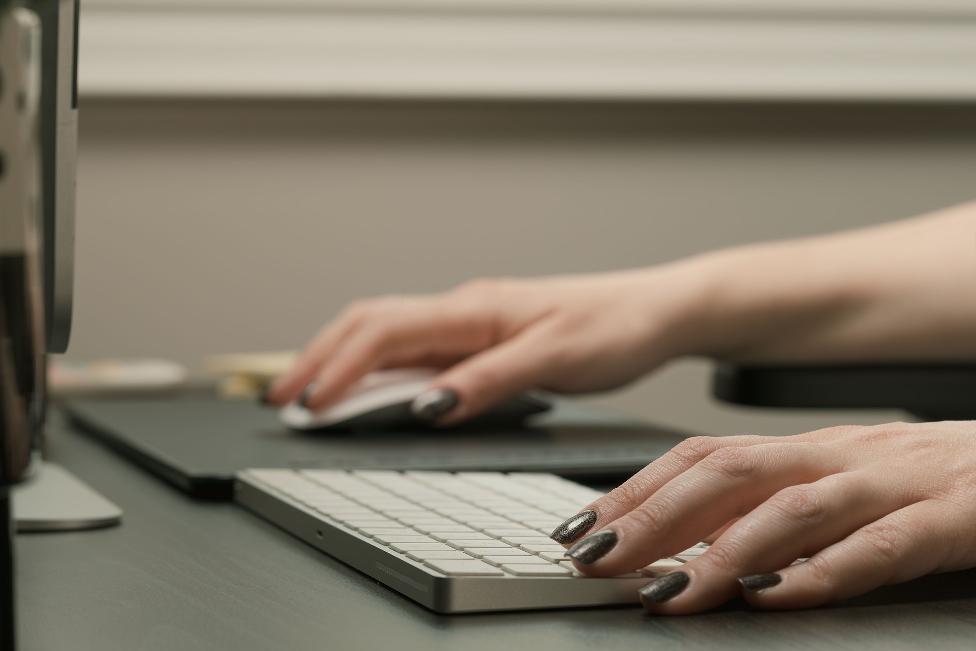 A woman is typing on a keyboard with a mouse